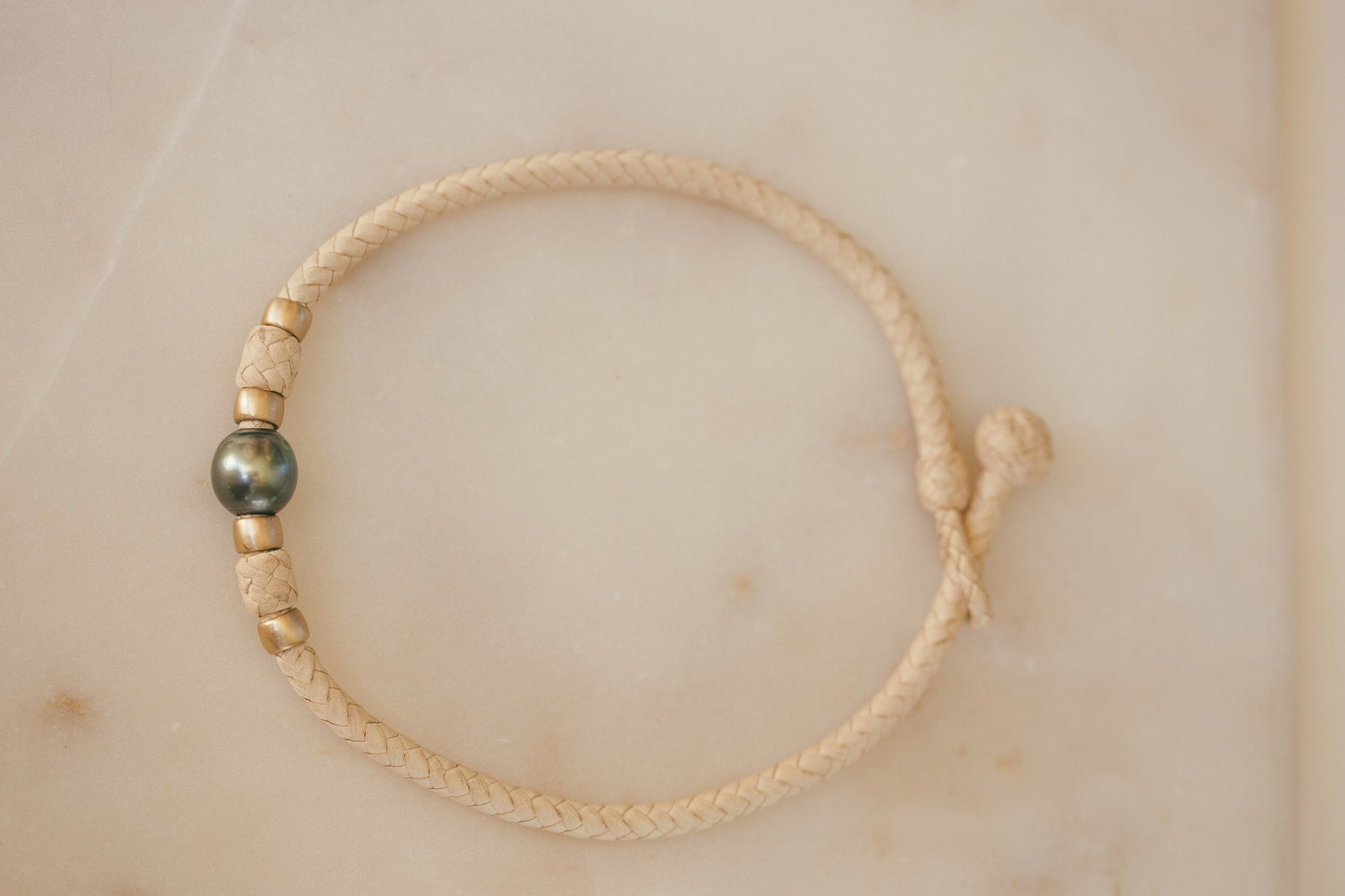 THE MOMI 14K GOLD CHOKER WITH TAHITIAN PEARL LAYING ON A PERL TABLE