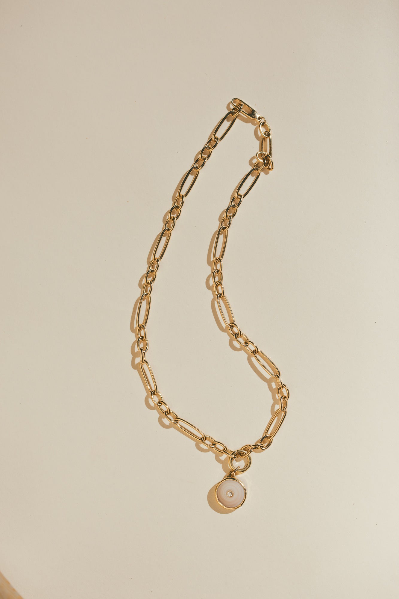 SMALL 18K GOLD PUKA CHARM WITH DIAMOND ONE-OF-A-KIND-WHITE LAYING ON A PLAIN BACKROUND