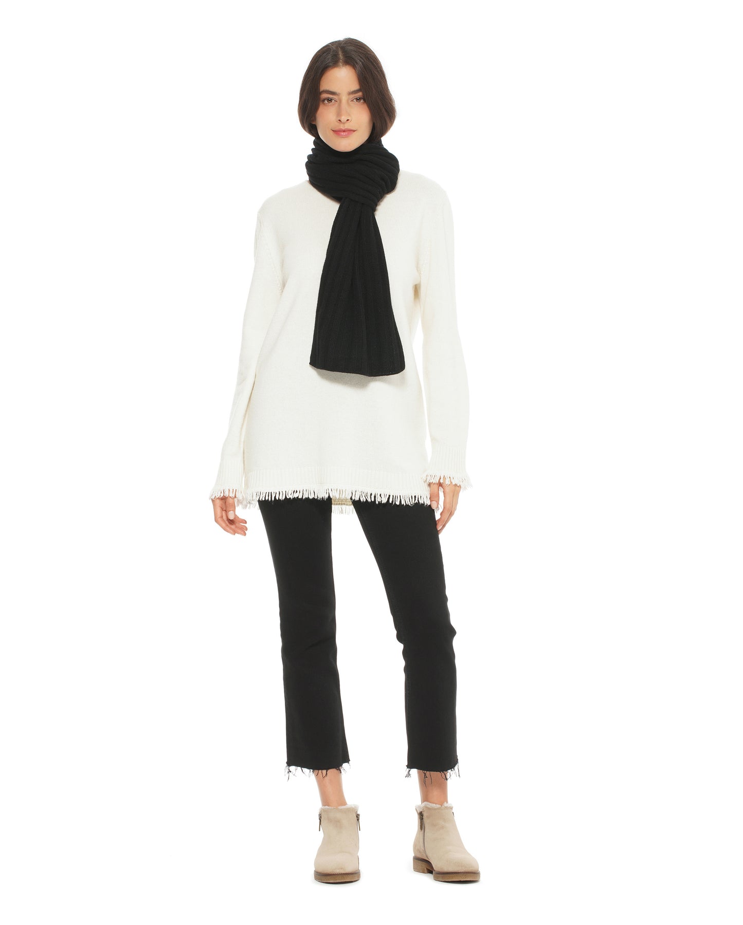 Person wearing a white sweater, black scarf, black pants, and beige boots on a white background