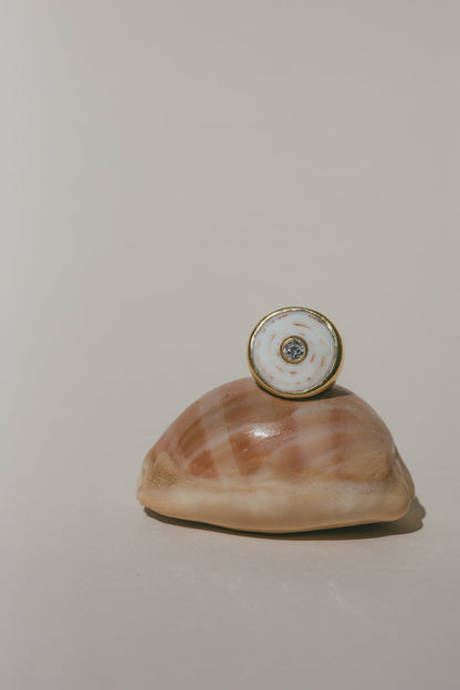 THE 18K GOLD PUKA RING WITH DIAMOND-ONE-OF-A-KIND-WHITE SITTING ON TOP OF A LIGHT BROWN SEA SHELL 