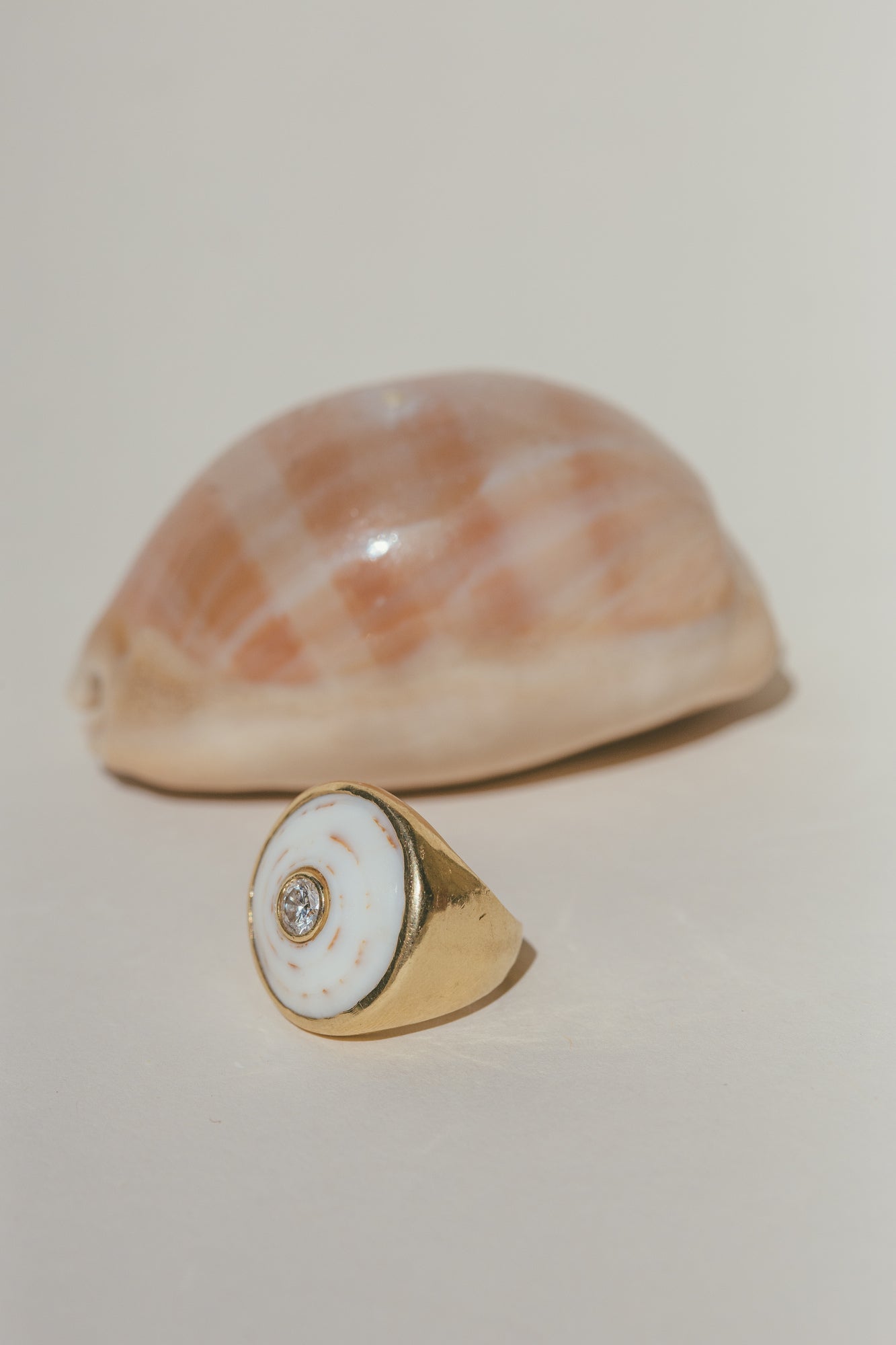 THE 18K GOLD PUKA RING WITH DIAMOND-ONE-OF-A-KIND-WHITE WITH A SEA SHELL BEHIND THE RING 