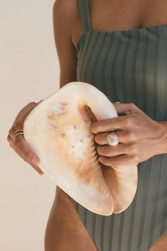 A FEMALE MODEL HOLDING A SEA SHELL WEARING THE 18K GOLD PUKA RING WITH DIAMOND-ONE-OF-A-KIND