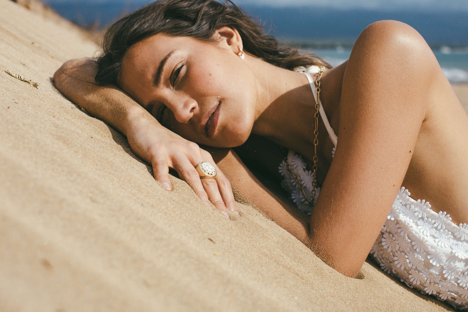 A MODEL LAYING ON BEACH SAND WEARING THE 18K GOLD PUKA RING-ONE-OF-A-KIND-PATTERN