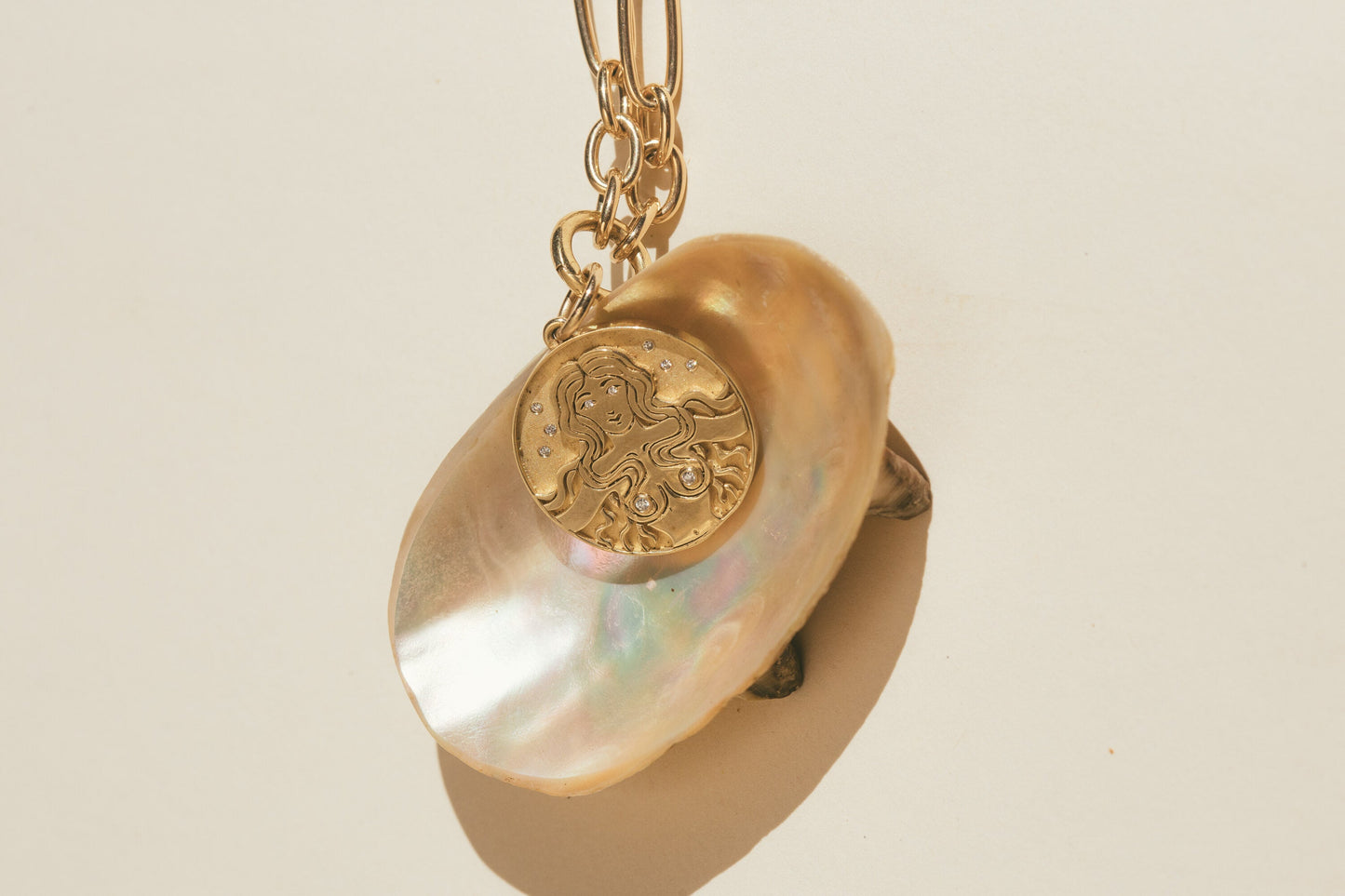 THE GOLD MERMAID DIAMOND CHARM ON TOP OF A SEA SHELL WITH THE SUN REFLECTING OFF THE SHELL