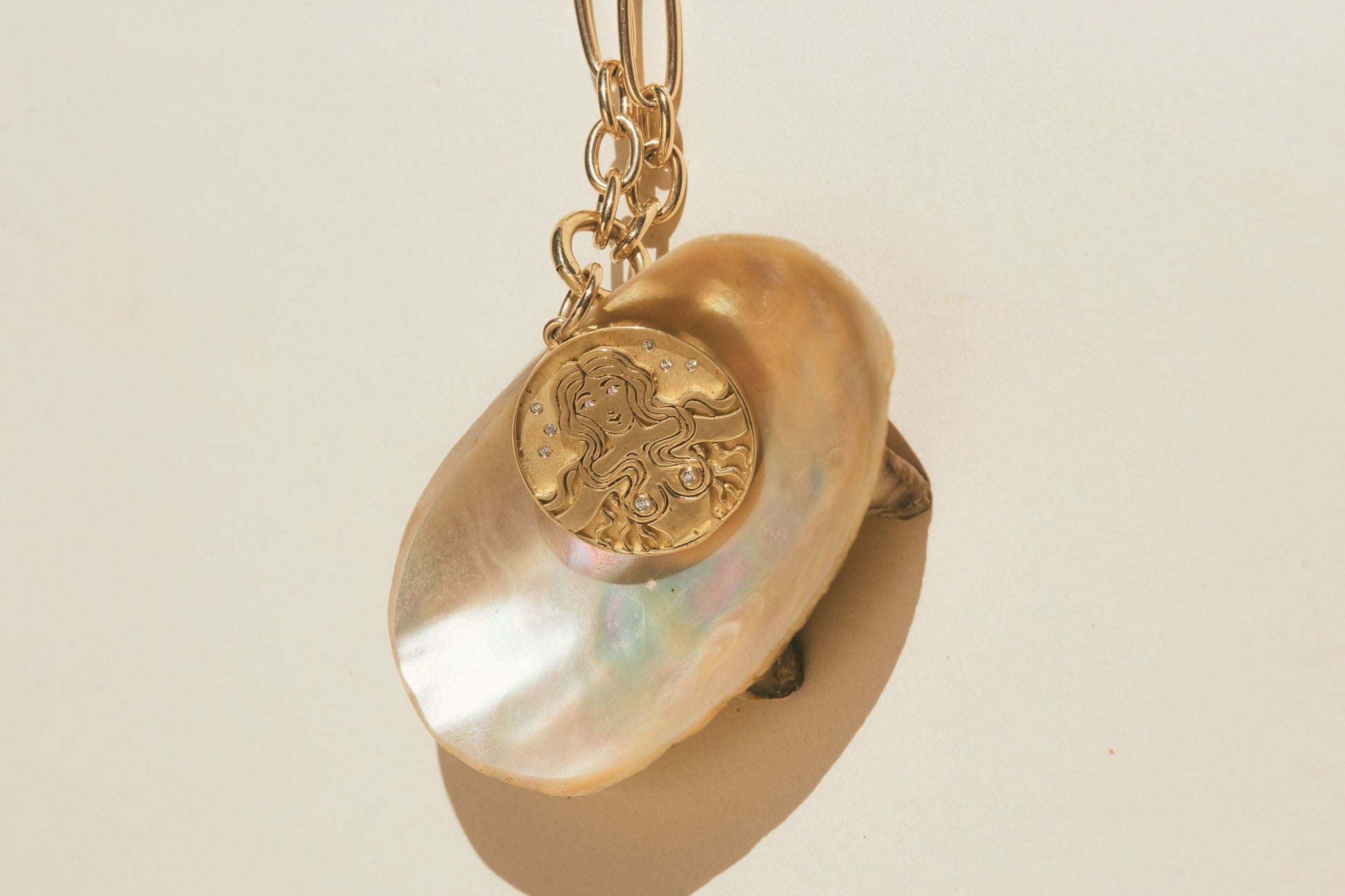 THE GOLD MERMAID DIAMOND CHARM ON TOP OF A SEA SHELL WITH THE SUN REFLECTING OFF THE SHELL