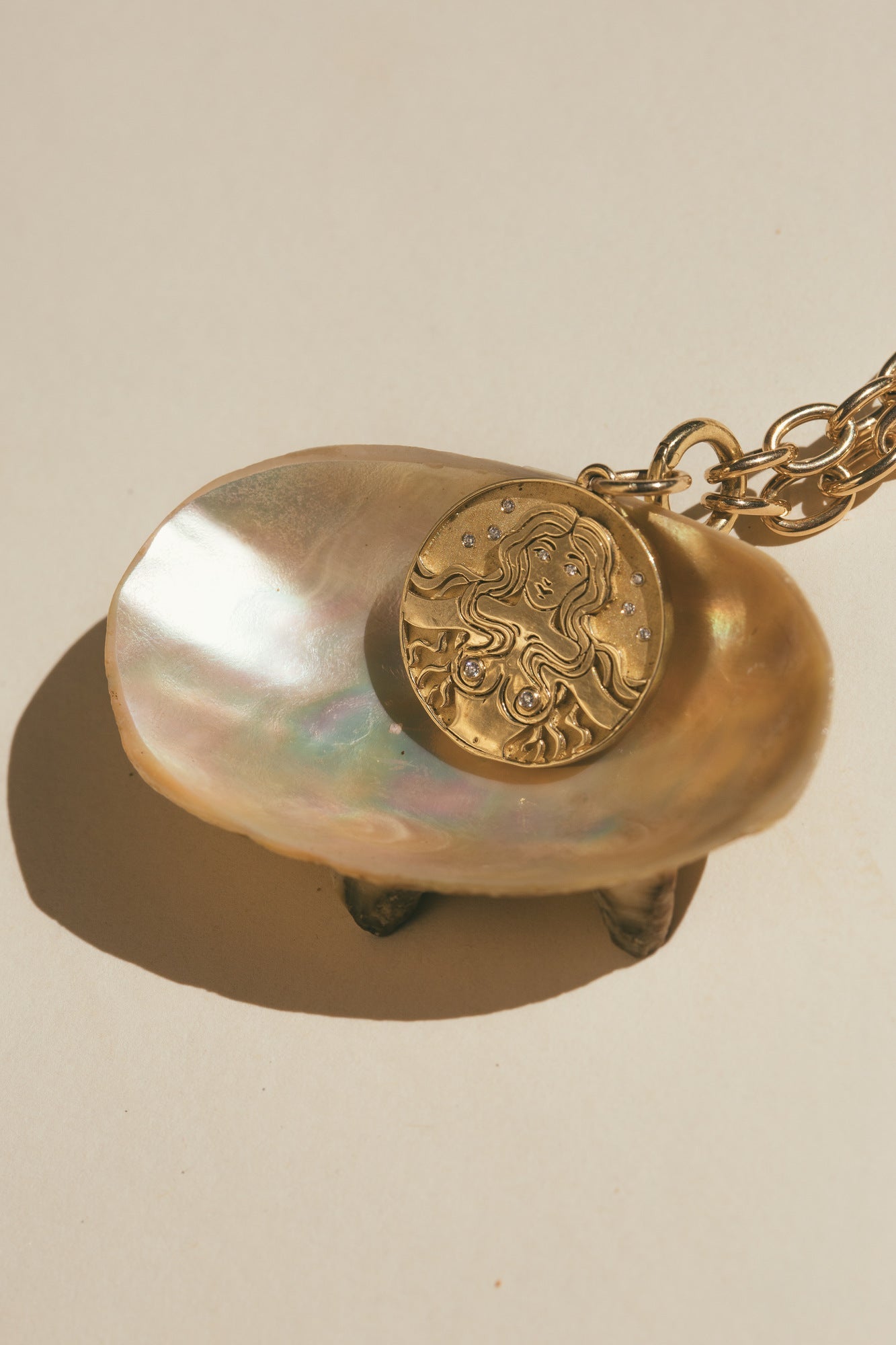 THE GOLD MERMAID DIAMOND CHARM ON TOP OF A LIGHT BROWN SEA SHELL