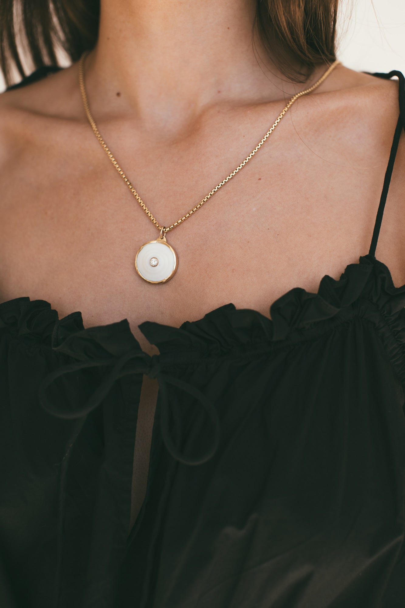 A CLOSE UP OF THEMEDIUM 18K GOLD PUKA CHARM WITH DIAMOND-ONE-OF-A-KIND-WHITE WITH A MODEL WEARING BLACK