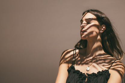 A SHADOW PHOTO OF A MODEL WEARING A MEDIUM 18K GOLD PUKA CHARM WITH DIAMOND-ONE-OF-A-KIND-WHITE