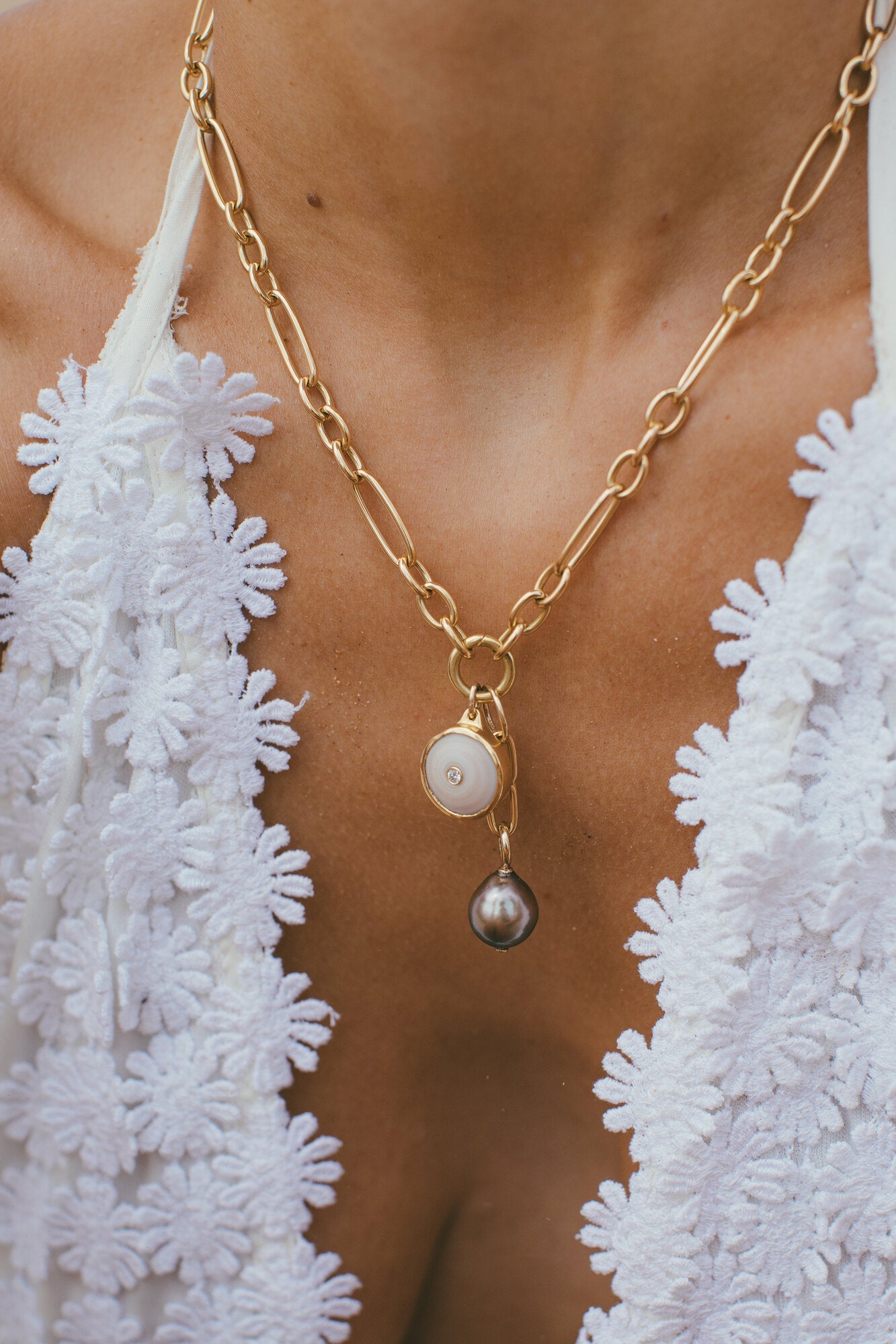 a close up of a model wearing SMALL 18K GOLD PUKA CHARM WITH DIAMOND ONE-OF-A-KIND-WHITE