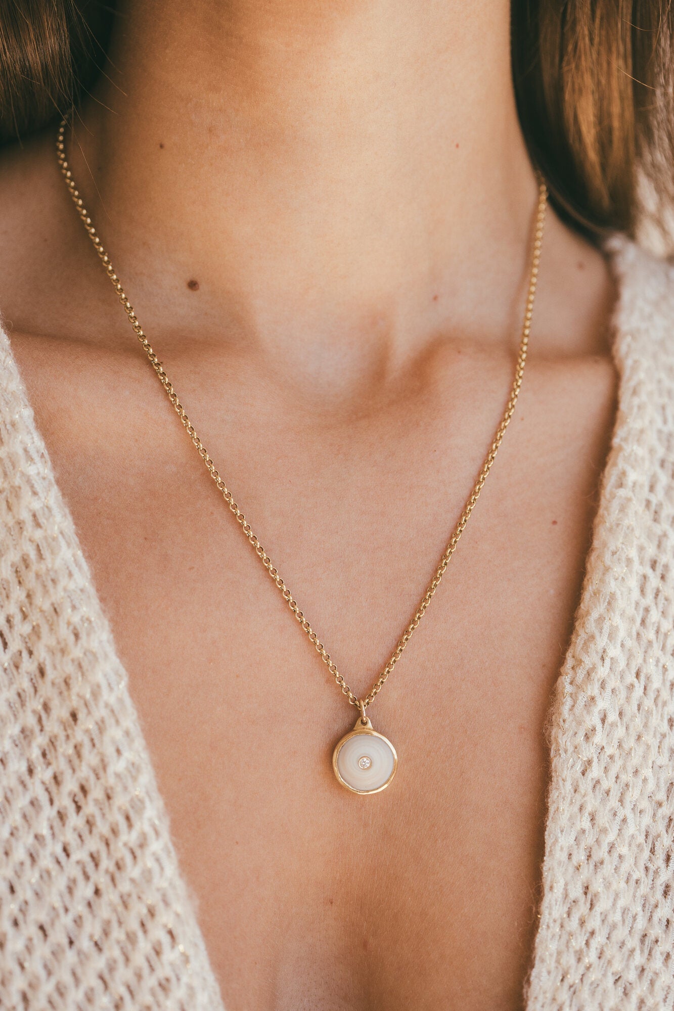 A CLOSE UP OF A MODEL WEARING A SMALL 18K GOLD PUKA CHARM WITH DIAMOND ONE-OF-A-KIND-WHITE