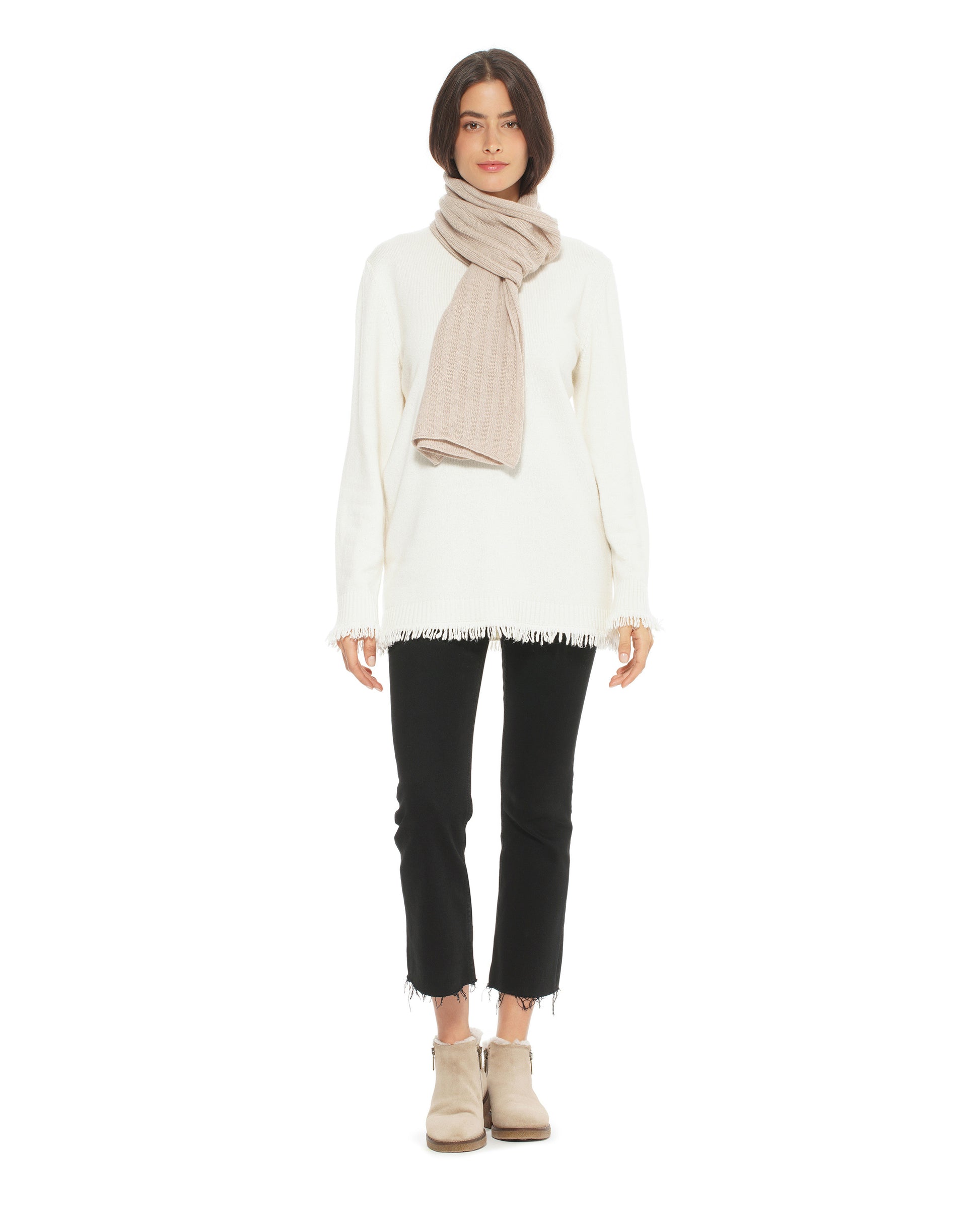 Person wearing a white sweater, black pants, and beige boots with a beige scarf on a white background