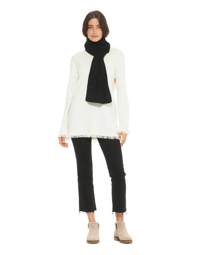 Person wearing a white sweater, black scarf, black pants, and beige boots on a white background